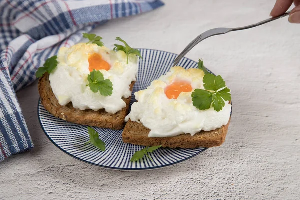 Una mano de mujer sostiene un tenedor sobre un plato de dieta Orsini de huevos batidos y horneados. Fondo claro. Desayuno de aristócratas franceses Imagen de stock