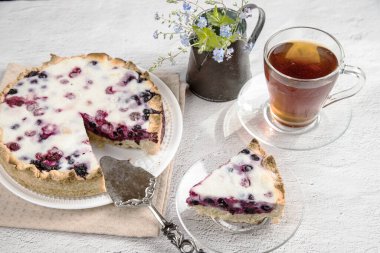 Parlak masanın üzerinde ev yapımı böğürtlenli turta ile birlikte beyaz bir tabak var. Ev çayı içme konsepti