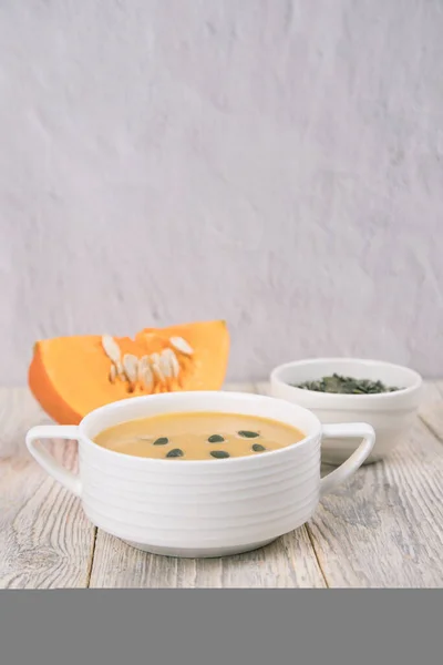 Tohumlar ve kesilmiş bir balkabağı parçasıyla beyaz bir fincanda kabak çorbası. Uzayı kopyala Sonbahar yemeği