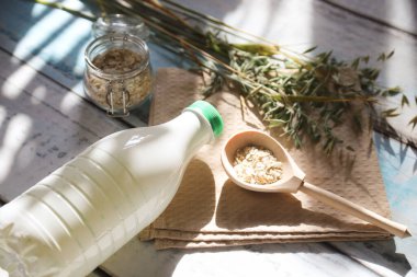 Tahta bir kaşık, yulaf gevreği ve masada güneş parlayan bir şişe yulaf sütü..