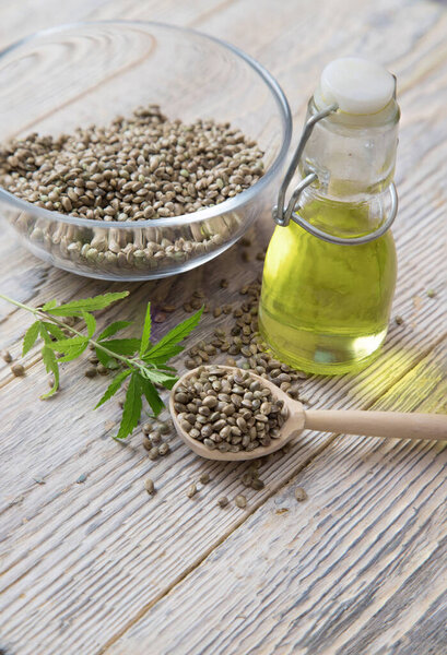 Масло конопли с семенами конопли в деревянной ложке и прозрачной пластине на светлом полу. Концепция альтернативных масел