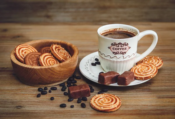 Há biscoitos, doces, ervilhas de chocolate, papoula; pires de porcelana e tampão com café, comida doce saborosa no fundo de madeira, tonificado — Fotografia de Stock