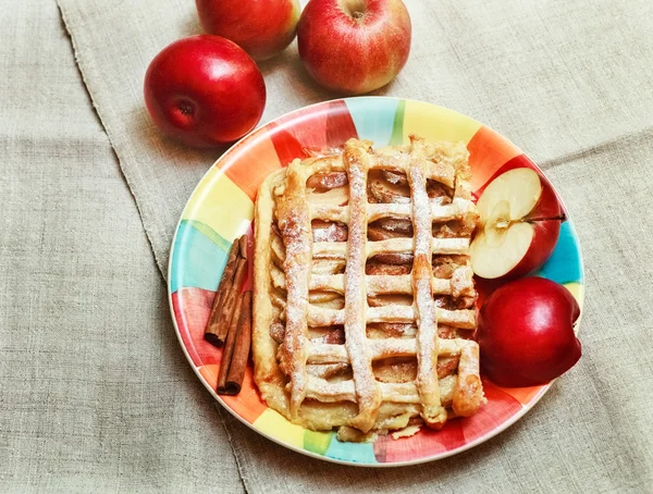 Tarte aux pommes avec grille de pâtisserie, poudre de sucre, sur la plaque en céramique avec cannelle et morceaux de pomme fraîche, vue du dessus — Photo