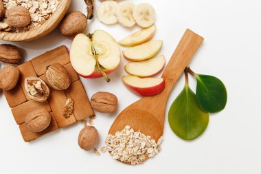 There are Banana,Apple,Orange with Walnuts in the Wooden Plate and Rolled Oats,Wooden Spoon,Trivet,with Green Leaves,Healthy Fresh Organic Food on the White Background,Selective Focus clipart