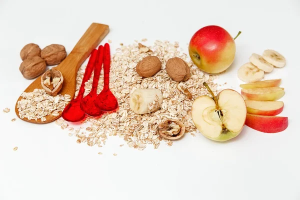 Er zijn stukken van banaan, appel, walnoten en Rolled Oats, houten en Plastic lepels, met groene bladeren, gezonde verse biologische voeding op de witte achtergrond — Stockfoto