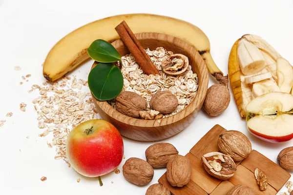 Υπάρχουν μπανάνα, μήλο, καρύδια στην ξύλινη πινακίδα και έλασης βρώμη ξύλινη Spoontrivet με πράσινο Leaves.Healthy φρέσκα βιολογικά τρόφιμα σε λευκό φόντο — Φωτογραφία Αρχείου