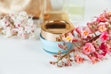 Orada beyaz ve pembe dalları kestane ağacı, altın kapak ile mavi şişe krem beyaz masaya vardır