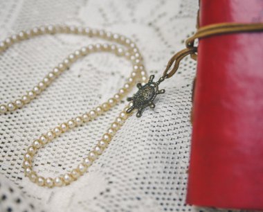 Kırmızı deri notebook ile beyaz perls dantel masa örtüsü vardır. Vintage tonlu arka plan