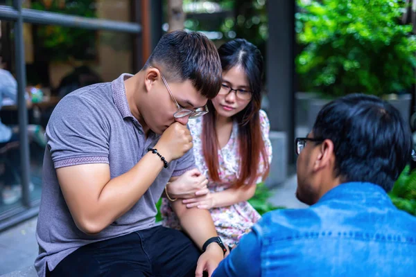 three asian friends sitting outside the office, over the shoulder view of a young Asian sad or stressed, his friends are comforting. Selective focus.