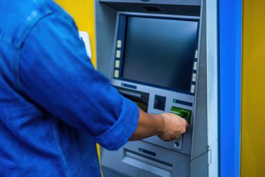 Bir adama yakın çekim (mavi kot pantolon giyen), ATM makinesinden para çekmek için kredi kartı kullanıyor. Finans ve iş konsepti. Seçici odak.