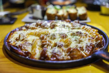 Tokbokki veya Tteokbokki (Baharatlı Pirinç Kekleri) peynirli baharatlı tavuk. Ahşap arka planda geleneksel Kore yemekleri yakın plan. Seçici odak.