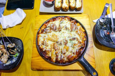 Tokbokki veya Tteokbokki (Baharatlı Pirinç Kekleri) peynirli baharatlı tavuk. Ahşap arka planda geleneksel Kore yemekleri yakın plan. Seçici odak.