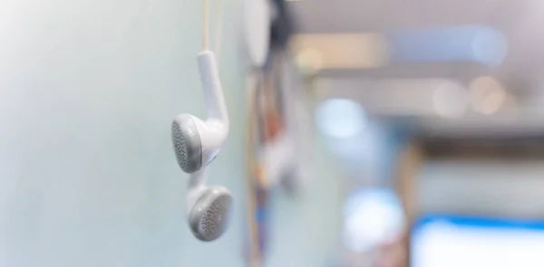 Banner of white earphones hanging off a office partitions. Modern earphones. A modern gadget on a blurred office background. Selective focus.