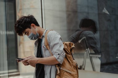Açık havada akıllı telefon kullanarak cerrahi maske takan Asyalı bir adam. Sağlık ve tıbbi konsept