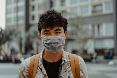 Cerrahi yüz maskesi takan Asyalı bir adam dışarıda ya da binanın önünde duruyor. Sağlık ve tıbbi konsept