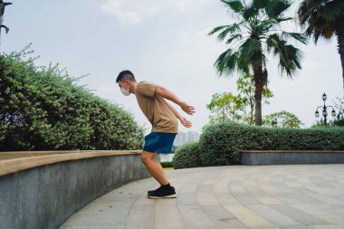 Sosyal uzaklık. Korumalı maskeli genç Asyalı adam dışarıda parkta çalışıyor. Egzersiz yap. Karantinada spor. Covid-19. Korunma. Seçici odak.