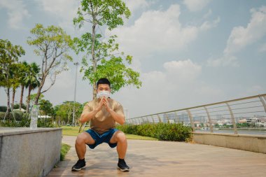Sosyal uzaklık. Korumalı maskeli genç Asyalı adam dışarıda parkta çalışıyor. Egzersiz yap. Karantinada spor. Covid-19. Korunma. Seçici odak.