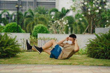 Sosyal uzaklık. Korumalı maskeli genç Asyalı adam dışarıda parkta çalışıyor. Egzersiz yap. Karantinada spor. Covid-19. Korunma. Seçici odak.