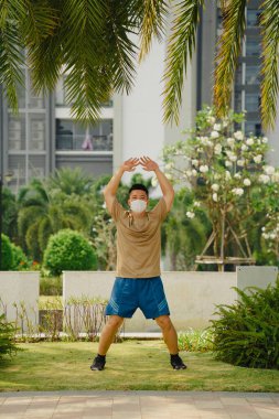 Sosyal uzaklık. Korumalı maskeli genç Asyalı adam dışarıda parkta çalışıyor. Egzersiz yap. Karantinada spor. Covid-19. Korunma. Seçici odak.