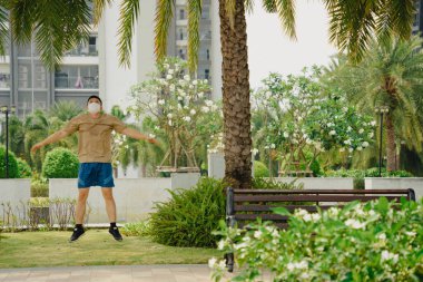 Sosyal uzaklık. Korumalı maskeli genç Asyalı adam dışarıda parkta çalışıyor. Egzersiz yap. Karantinada spor. Covid-19. Korunma. Seçici odak.