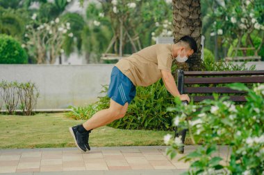 Sosyal uzaklık. Korumalı maskeli genç Asyalı adam dışarıda parkta çalışıyor. Egzersiz yap. Karantinada spor. Covid-19. Korunma. Seçici odak.