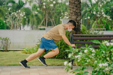 Sosyal uzaklık. Korumalı maskeli genç Asyalı adam dışarıda parkta çalışıyor. Egzersiz yap. Karantinada spor. Covid-19. Korunma. Seçici odak.