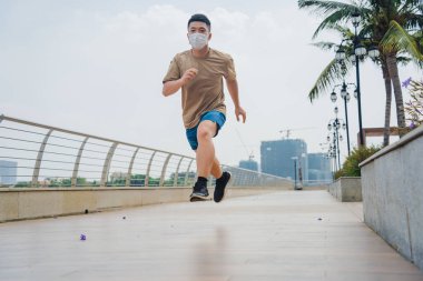 Koşarken ve parkta koşarken yüz maskesi takan Asyalı genç bir sporcu. Seçici odak.