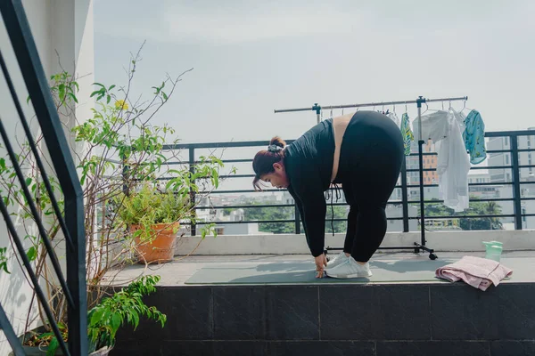 Health, fitness and sports concept. Plus size young asian woman doing exercise on mat in balcony, going to loose extra pounds at home, become strong and fit, training endurance. Social distancing.