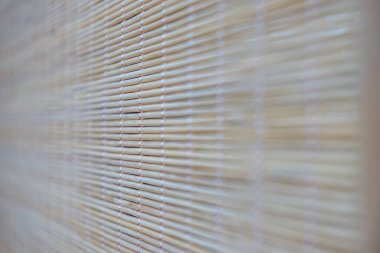 Arka plan olarak birbirine geçmiş bambu parçacıklarından oluşan bir hasırın parçası. Bej bambuların yakın plan ahşap arka planı. Doğu tarzında tasarımcı geçmişi. Seçici odak.