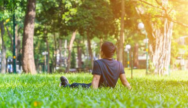 Genç Asyalı adam yeşil çimlerde oturuyor ve kulaklıkla kulaklıkla müzik dinliyor açık havada cep telefonundan, doğanın tadını çıkarıyor, kopyalama alanı, seçici odaklanma