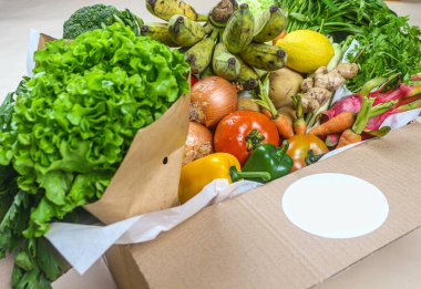 Close-up of fresh vegetables in cardboard box on the table delivered to home, donation box with supplies food for people, vegetables and fruit in cardboard box. Selective focus.
