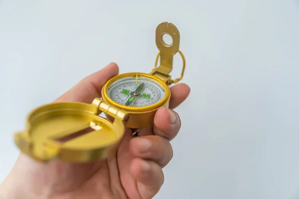 Hand holding golden compass isolated, shallow DOF, focus on dial. Compass on a white background. Concept for direction, travel, guidance or assistance. Selective focus.