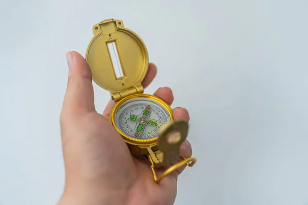 Hand holding golden compass isolated, shallow DOF, focus on dial. Compass on a white background. Concept for direction, travel, guidance or assistance. Selective focus.