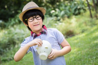 Küçük Asyalı çocuk ayakta ve onun kumbara park holding