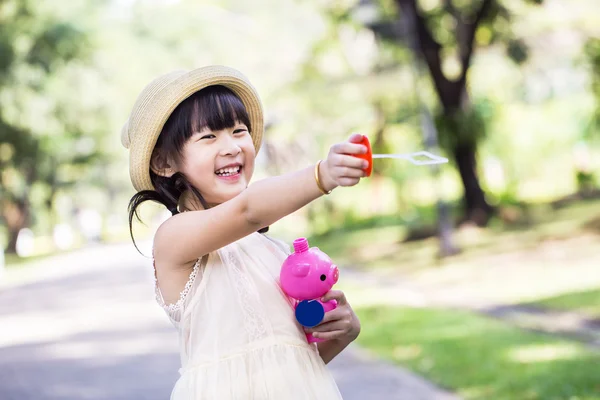 Asiática niña está soplando un jabón burbujas con sonrisa cara en p — Foto de Stock