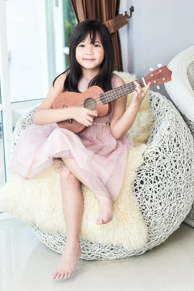 Piccolo asiatico carino ragazza giocare legno ukulele su bianco trama sof Foto Stock Royalty Free