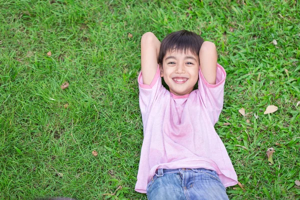 Pequeño niño acostado en la hierba con la cara sonriente — Foto de Stock