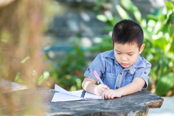 Маленький азиатский мальчик пишет карандашом на блокноте — стоковое фото