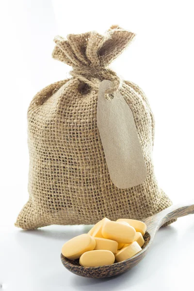 Pilules jaunes dans un sac de toile de jute vide et sur une cuillère — Photo