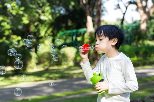 Asiático pequeño chico es soplando un jabón burbujas en parque — Foto de Stock