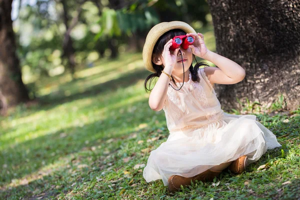 Little asian girl looking trough a binoculars in park — Stock Photo, Image