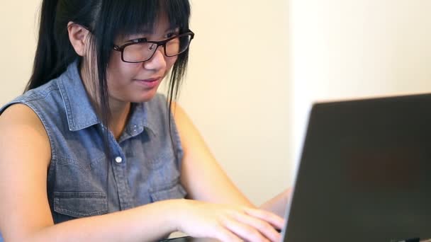 Азіатський жінка в окулярах, сидячи на стілець вдома і вона працює на ноутбуці — стокове відео