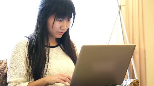 Asiática mujer sentada en silla en casa y ella trabaja en un ordenador portátil — Vídeo de stock