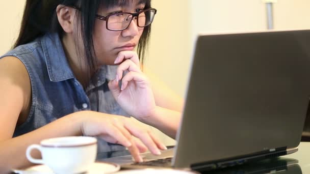 Asiatique femme portant des lunettes assis sur la chaise à la maison et elle travaille sur un ordinateur portable — Video