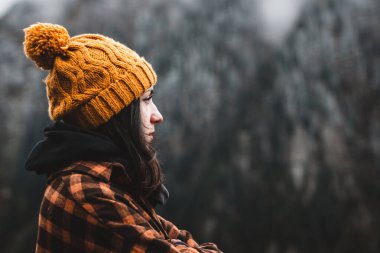 Soğuk hava koşullarında manzaraya bakan ekose gömlekli ve sarı şapkalı düşünceli genç bir kadın. Seyahat, açık hava ve soğuk hava konsepti. Boşluğu Kopyala