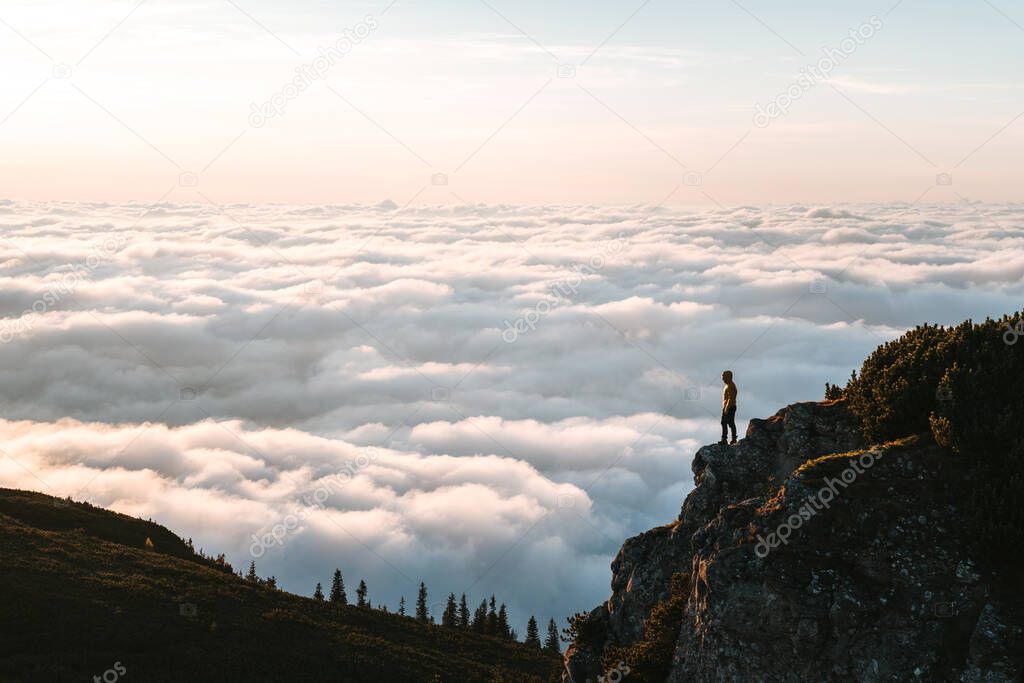 Hiker standing on cliff edge and looking at view on montain summit. Young climber enjoying sunrise or sunset looking at the cloud inversion. Travel, sport and active life concept in Ceahlau Massiff
