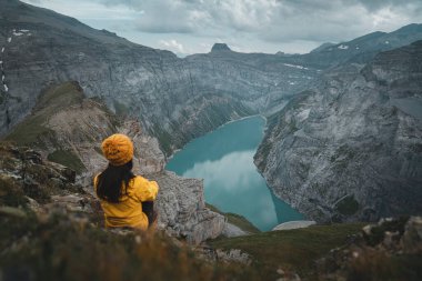 Sarı ceketli genç bir kadın dağın tepesinde dikilip Limmernsee Gölü 'ne bakıyor. Dişi dağ yamacında oturuyor ve Glarus, İsviçre 'nin güzel manzarasının tadını çıkarıyor.