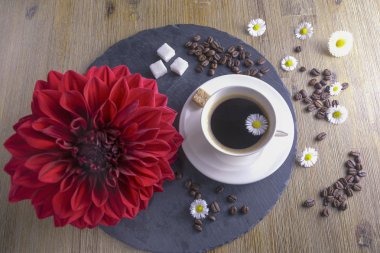 Siyah çay siyah ve kahverengi bir arka plan ile yapılan kompozisyon. Kırmızı çiçek, şeker, papatya ve kahve çekirdekleri ile siyah kahve fincan. Bu simbolizes güzel sabah lezzetli çay ile.
