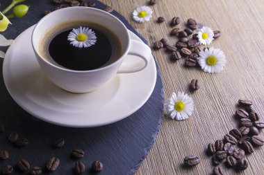 Siyah çay siyah ve kahverengi bir arka plan ile yapılan kompozisyon. Beyaz çiçek, papatya ve kahve çekirdekleri ile siyah kahve fincan. Bu simbolizes güzel sabah lezzetli çay ile.