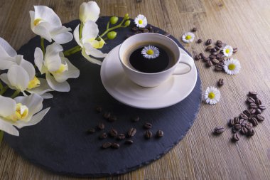 Siyah çay siyah ve kahverengi bir arka plan ile yapılan kompozisyon. Beyaz çiçek, papatya ve kahve çekirdekleri ile siyah kahve fincan. Bu simbolizes güzel sabah lezzetli çay ile.